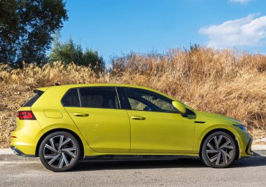 Inca, İspanya - 21 Temmuz 2025: İnka, İspanya 'da yol kenarında güneşli bir gökyüzünün altında çimen ve ağaçlarla parlayan parlak yeşil bir Volkswagen Golf' ün yan görüntüsü