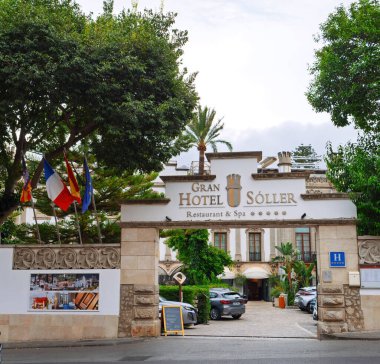Soller, İspanya - 24 Temmuz 2025: Mallorca İspanya 'da bir restoran ve kaplıcaya ev sahipliği yapan tarihi bir binanın önünde, bayraklı, ağaçlı ve park halindeki Gran Hotel Soller girişinin sokak manzarası