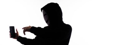 Hacker Anonymous and face mask with smartphone in hand. Man in black hood shirt holding and using mobile phone on white background. Represent cyber crime data hacking or stealing personal data concept