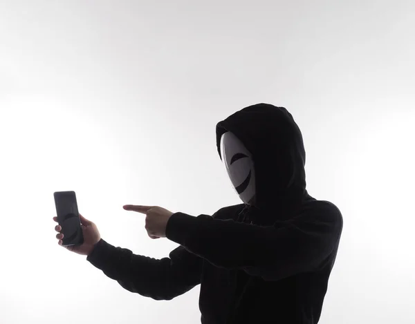 Hacker Anonymous and face mask with smartphone in hand. Man in black hood shirt holding and using mobile phone on white background. Represent cyber crime data hacking or stealing personal data concept