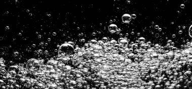 Soda su kabarcıkları siyah arka planda su altında sıçrıyor. Karbonat içeceği konseptini canlandırmak için suyun altında bir patlama gibi köpüren ve yüzeye doğru yüzen kola sıvısı dokusu..