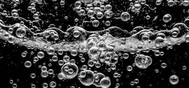 Soda su kabarcıkları siyah arka planda su altında sıçrıyor. Karbonat içeceği konseptini canlandırmak için suyun altında bir patlama gibi köpüren ve yüzeye doğru yüzen kola sıvısı dokusu..