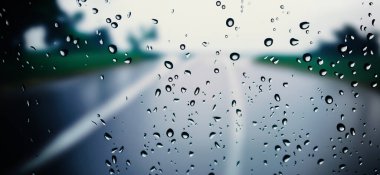 Araba ön camına veya araba camına yağmur yağacak ve arka planda bulanık bir yol olacak. Yağmur mevsiminde araba sürüyorum. Araba aynasına yağmur damlaları düşer. Akşam yağmurunda trafik yolu. Çiseleme yağmuru araba sürmeyi azaltır