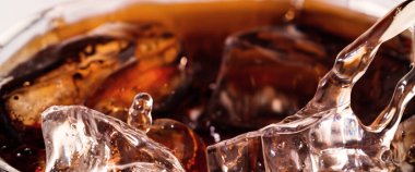 Kola ve buz dökülüyor. Kola soda ve buz fışkırıyor ya da yüzeye çıkıyor. Kola suyundaki buzu kapat. Bardakta kabarcıklar olan karbonat içeceği. Soğuk içecek arka planı