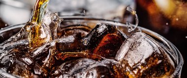Kola ve buz dökülüyor. Kola soda ve buz fışkırıyor ya da yüzeye çıkıyor. Kola suyundaki buzu kapat. Bardakta kabarcıklar olan karbonat içeceği. Soğuk içecek arka planı