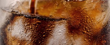 Kola ve buz dökülüyor. Kola soda ve buz fışkırıyor ya da yüzeye çıkıyor. Kola suyundaki buzu kapat. Bardakta kabarcıklar olan karbonat içeceği. Soğuk içecek arka planı