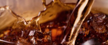 Kola ve buz dökülüyor. Kola soda ve buz fışkırıyor ya da yüzeye çıkıyor. Kola suyundaki buzu kapat. Bardakta kabarcıklar olan karbonat içeceği. Soğuk içecek arka planı
