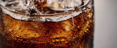 Kola ve buz dökülüyor. Kola soda ve buz fışkırıyor ya da yüzeye çıkıyor. Kola suyundaki buzu kapat. Bardakta kabarcıklar olan karbonat içeceği. Soğuk içecek arka planı