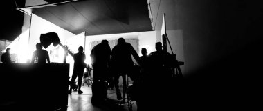 Film stüdyosunda profosyonel ışık ve kamera ekipmanları ve film yönetmeniyle profesyonel film ekibinin yer aldığı video prodüksiyon sahnelerinin silueti.