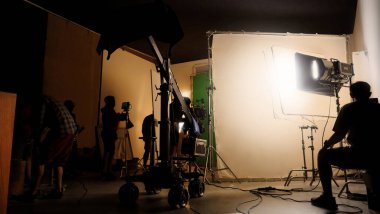 Film stüdyosunda profosyonel ışık ve kamera ekipmanları ve film yönetmeniyle profesyonel film ekibinin yer aldığı video prodüksiyon sahnelerinin silueti.