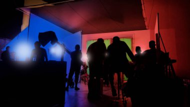 Film stüdyosunda profosyonel ışık ve kamera ekipmanları ve film yönetmeniyle profesyonel film ekibinin yer aldığı video prodüksiyon sahnelerinin silueti.