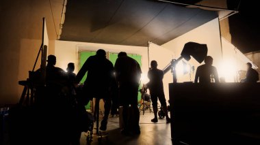 Film stüdyosunda profosyonel ışık ve kamera ekipmanları ve film yönetmeniyle profesyonel film ekibinin yer aldığı video prodüksiyon sahnelerinin silueti.