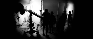 Film stüdyosunda profosyonel ışık ve kamera ekipmanları ve film yönetmeniyle profesyonel film ekibinin yer aldığı video prodüksiyon sahnelerinin silueti.
