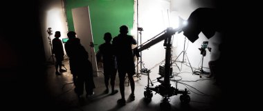 Film stüdyosunda profosyonel ışık ve kamera ekipmanları ve film yönetmeniyle profesyonel film ekibinin yer aldığı video prodüksiyon sahnelerinin silueti.