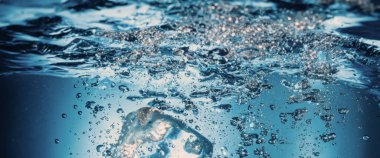 Su sıçratma ve buz küpü. Bir bardak suya buz sıçrıyor. Su altı buz küpleri berrak sulama arka planına dökülüyor. Serinletici bir içecek. Mavi arka planı olan bir bardaktaki buzlar