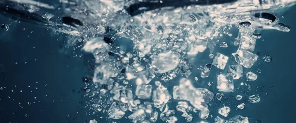 Water splashing and ice cube. Ice splashing into a glass of water. Underwater pouring ice cubes falling into clear watering background. Refreshing chill drinking. Ices in a glass with blue background