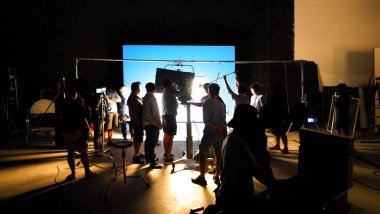 Tv reklam filmi çekimleri sahnesinin arkasındaki video görüntülerinin silueti. Film ekibi Lightman ve kameraman büyük stüdyoda yönetmen ve ekipman ile birlikte çalışıyorlar..