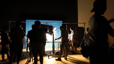 Tv reklam filmi çekimleri sahnesinin arkasındaki video görüntülerinin silueti. Film ekibi Lightman ve kameraman büyük stüdyoda yönetmen ve ekipman ile birlikte çalışıyorlar..