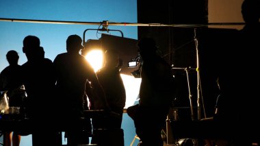 Tv reklam filmi çekimleri sahnesinin arkasındaki video görüntülerinin silueti. Film ekibi Lightman ve kameraman büyük stüdyoda yönetmen ve ekipman ile birlikte çalışıyorlar..