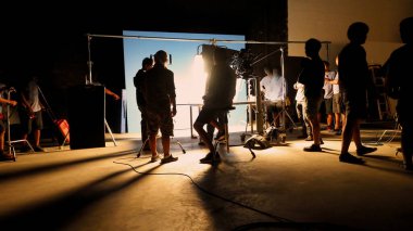 Tv reklam filmi çekimleri sahnesinin arkasındaki video görüntülerinin silueti. Film ekibi Lightman ve kameraman büyük stüdyoda yönetmen ve ekipman ile birlikte çalışıyorlar..