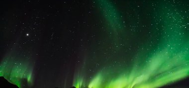 Aurora australis veya Aurora borealis veya yeşil kuzey ışıkları dağların üzerinde gökyüzü. Kutup ışıklarıyla gece gökyüzü. Güney ışıkları ve gerçek doğal kara arka plana karşı gece manzarası..