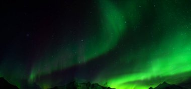 Aurora australis veya Aurora borealis veya yeşil kuzey ışıkları dağların üzerinde gökyüzü. Kutup ışıklarıyla gece gökyüzü. Güney ışıkları ve gerçek doğal kara arka plana karşı gece manzarası..