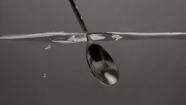 Bar kaşığıyla içki karıştırmak. Gümüş metal kaşık suları Votka Cin veya tekila gibi alkollü içecekleri karıştırır. Barmen kaşığı temiz suyun altında gri arka planda.