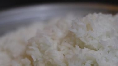 Yakın plan, pilav pişirme makinesinden plastik bir pirinç küreğiyle çıkartılan taze pişmiş beyaz pirinç. Tayland 'ın yumuşak dokusu tanecikleri eritiyor. Ev yapımı pilav pişirme yemekleri. Slow Motion görüntüleri.