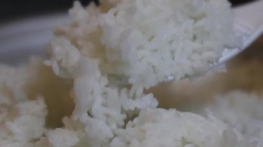Yakın plan, pilav pişirme makinesinden plastik bir pirinç küreğiyle çıkartılan taze pişmiş beyaz pirinç. Tayland 'ın yumuşak dokusu tanecikleri eritiyor. Ev yapımı pilav pişirme yemekleri. Slow Motion görüntüleri.