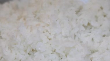 Yakın plan, pilav pişirme makinesinden plastik bir pirinç küreğiyle çıkartılan taze pişmiş beyaz pirinç. Tayland 'ın yumuşak dokusu tanecikleri eritiyor. Ev yapımı pilav pişirme yemekleri. Slow Motion görüntüleri.