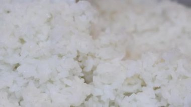 Yakın plan, pilav pişirme makinesinden plastik bir pirinç küreğiyle çıkartılan taze pişmiş beyaz pirinç. Tayland 'ın yumuşak dokusu tanecikleri eritiyor. Ev yapımı pilav pişirme yemekleri. Slow Motion görüntüleri.