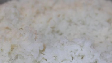 Yakın plan, pilav pişirme makinesinden plastik bir pirinç küreğiyle çıkartılan taze pişmiş beyaz pirinç. Tayland 'ın yumuşak dokusu tanecikleri eritiyor. Ev yapımı pilav pişirme yemekleri. Slow Motion görüntüleri.