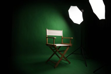 Yeşil ekran arka planlı fotoğraf stüdyosu ve profesyonel ışıklandırma ekipmanlarına karşı ahşap tabure. Profesyonel ışıklandırma ekipmanlarıyla fotoğraf stüdyosunun içi ve yeşil arka planlı yönetmen koltuğu.