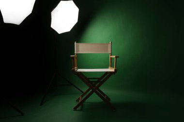 Yeşil ekran arka planlı fotoğraf stüdyosu ve profesyonel ışıklandırma ekipmanlarına karşı ahşap tabure. Profesyonel ışıklandırma ekipmanlarıyla fotoğraf stüdyosunun içi ve yeşil arka planlı yönetmen koltuğu.