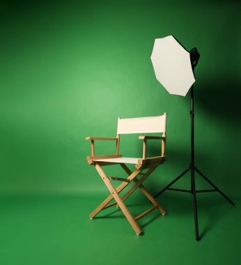 Yeşil ekran arka planlı fotoğraf stüdyosu ve profesyonel ışıklandırma ekipmanlarına karşı ahşap tabure. Profesyonel ışıklandırma ekipmanlarıyla fotoğraf stüdyosunun içi ve yeşil arka planlı yönetmen koltuğu.