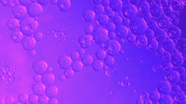 Petrol baloncukları soyut arka planda hareket eder. Renk sıvısı içinde yüzen berrak yağ kabarcıklarının hareketi. Rahatlatıcı ve sanatsal görsel deneyim. Petrol ve sudan akıcılık bilimini sembolize ediyor.