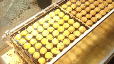 Japon Takoyaki yemekleri. Bir sokak yemeği şefi taze pişmiş takoyaki hazırlıyor. Japonya Takoyaki içi doğranmış ahtapotla dolu hamurdan yapıldı ve sıcak servis edildi. Şef altın Tako toplarını tepsiye koyar..