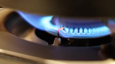 Gaz ocağı alevi. Gaz sobasını kapat ve mavi bir ateşle tutuştur. Ateşleme elektrodu, ateşi yakarken kırmızı bir şekilde parlar. Mutfak gaz sobasında kontrollü yanma sürecini gösterir.