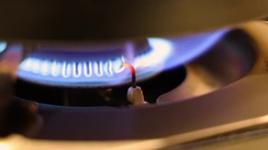 Gaz ocağı alevi. Gaz sobasını kapat ve mavi bir ateşle tutuştur. Ateşleme elektrodu, ateşi yakarken kırmızı bir şekilde parlar. Mutfak gaz sobasında kontrollü yanma sürecini gösterir.