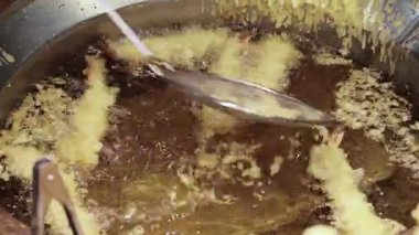 Karides tempura. Sıcak yağda kızartılmış karides tempurasına yakın çekim. Tong köpüren tavadan çıtır çıtır bir parça kaldırıyor. Altın hamuru kıtır kıtır kıtır kıtır yapar. Kızarmış tempura Osaka Japonya.