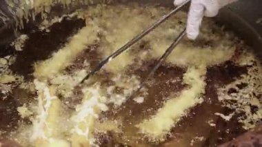 Karides tempura. Sıcak yağda kızartılmış karides tempurasına yakın çekim. Tong köpüren tavadan çıtır çıtır bir parça kaldırıyor. Altın hamuru kıtır kıtır kıtır kıtır yapar. Kızarmış tempura Osaka Japonya.