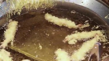 Karides tempura. Sıcak yağda kızartılmış karides tempurasına yakın çekim. Tong köpüren tavadan çıtır çıtır bir parça kaldırıyor. Altın hamuru kıtır kıtır kıtır kıtır yapar. Kızarmış tempura Osaka Japonya.