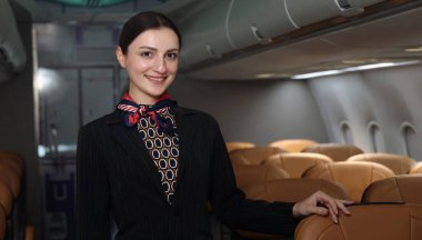 Hostes. Üniformalı gülen uçuş görevlisi modern bir uçağa binen yolcuları karşılıyor ve onlara rehberlik ediyor. Arkadaş canlısı havayolu personeli profesyonel hizmet ve konforlu uçuş deneyimi sunuyor