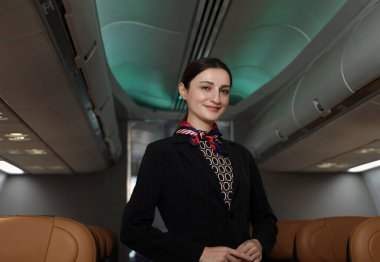 Hostes. Üniformalı gülen uçuş görevlisi modern bir uçağa binen yolcuları karşılıyor ve onlara rehberlik ediyor. Arkadaş canlısı havayolu personeli profesyonel hizmet ve konforlu uçuş deneyimi sunuyor