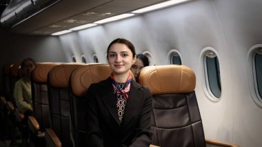 Hostes. Üniformalı gülen uçuş görevlisi modern bir uçağa binen yolcuları karşılıyor ve onlara rehberlik ediyor. Arkadaş canlısı havayolu personeli profesyonel hizmet ve konforlu uçuş deneyimi sunuyor