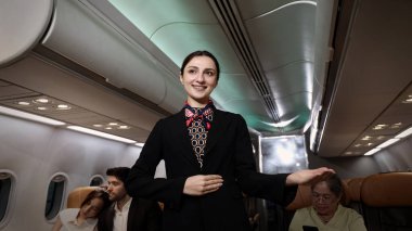 Hostes. Üniformalı gülen uçuş görevlisi modern bir uçağa binen yolcuları karşılıyor ve onlara rehberlik ediyor. Arkadaş canlısı havayolu personeli profesyonel hizmet ve konforlu uçuş deneyimi sunuyor
