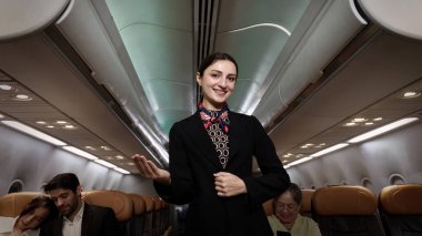 Hostes. Üniformalı gülen uçuş görevlisi modern bir uçağa binen yolcuları karşılıyor ve onlara rehberlik ediyor. Arkadaş canlısı havayolu personeli profesyonel hizmet ve konforlu uçuş deneyimi sunuyor