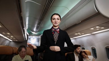 Hostes. Üniformalı gülen uçuş görevlisi modern bir uçağa binen yolcuları karşılıyor ve onlara rehberlik ediyor. Arkadaş canlısı havayolu personeli profesyonel hizmet ve konforlu uçuş deneyimi sunuyor