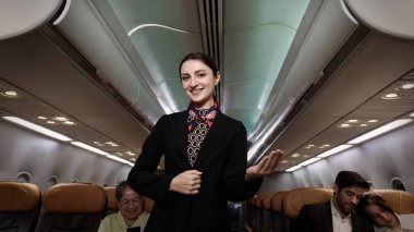 Hostes. Üniformalı gülen uçuş görevlisi modern bir uçağa binen yolcuları karşılıyor ve onlara rehberlik ediyor. Arkadaş canlısı havayolu personeli profesyonel hizmet ve konforlu uçuş deneyimi sunuyor