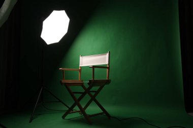 Film yönetmeni. Softbox ışıklandırmalı yeşil ekran stüdyo kurulumunda yönetmen koltuğu. Film yapımı video çekimi için ideal fotoğraf röportajları ve yeşil renkli anahtar arka planlı yaratıcı içerik
